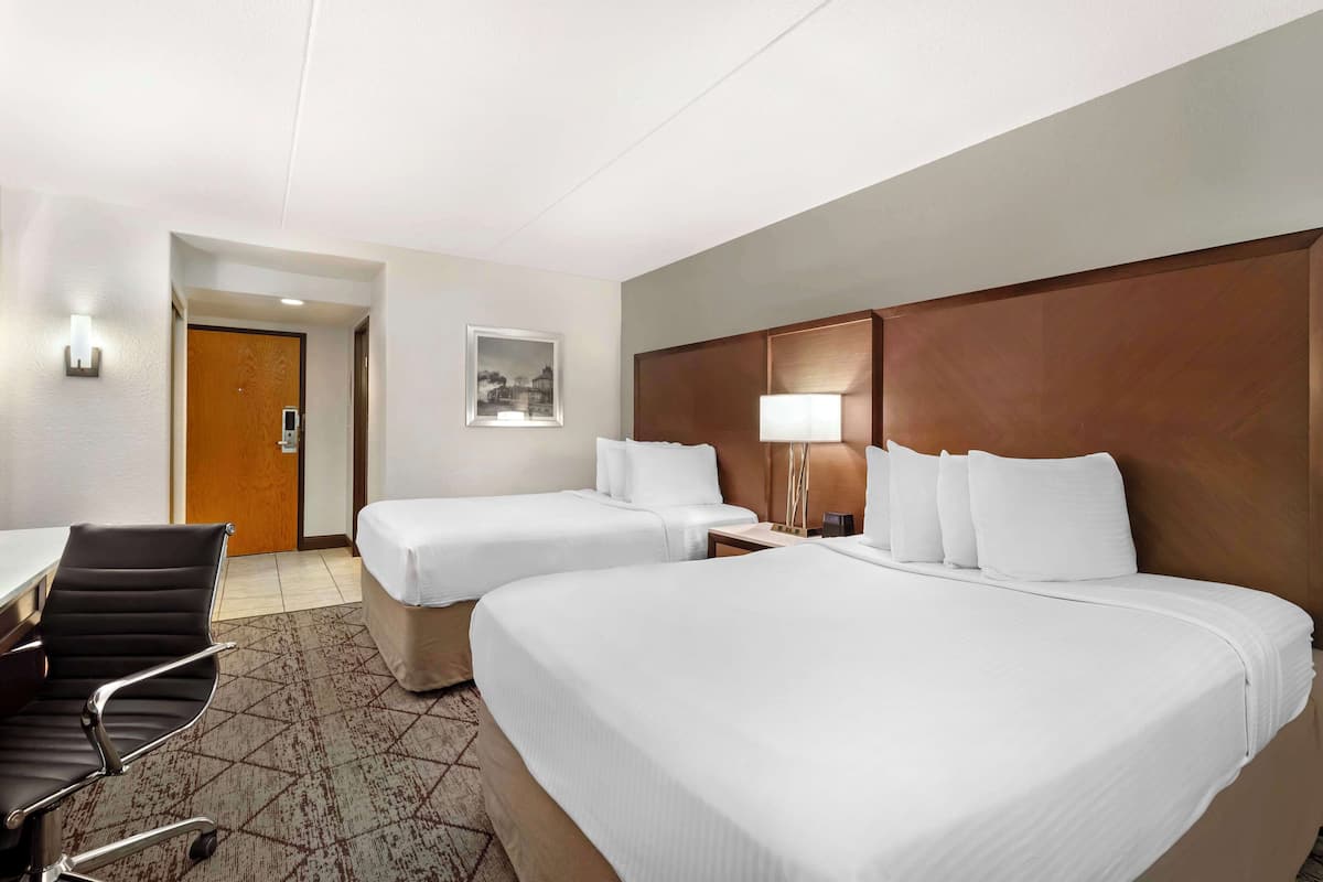 A hotel room with two beds, a desk, a chair, a lamp, and a door.