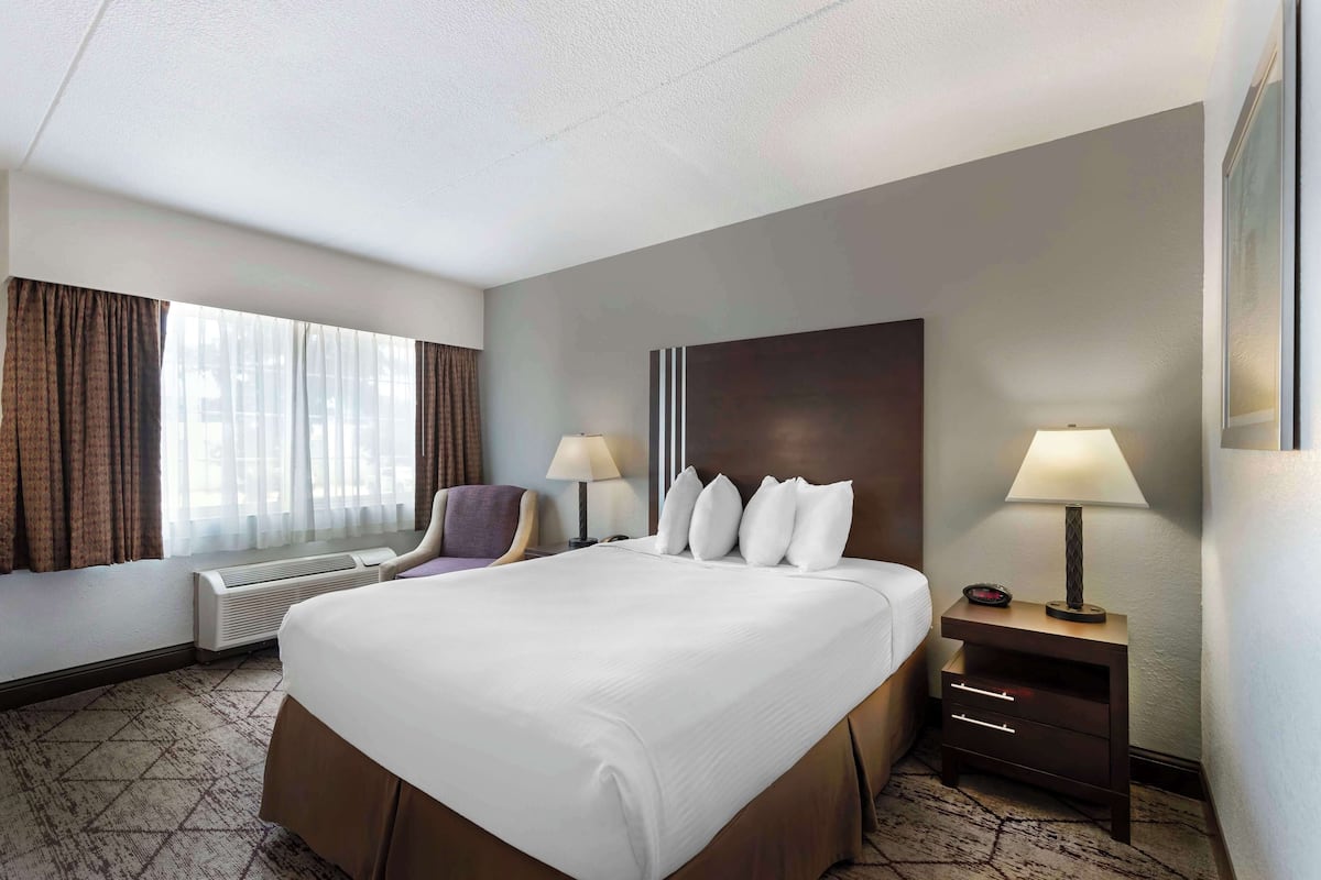 A hotel room with a large bed, two bedside tables with lamps, a chair, and a window with curtains.