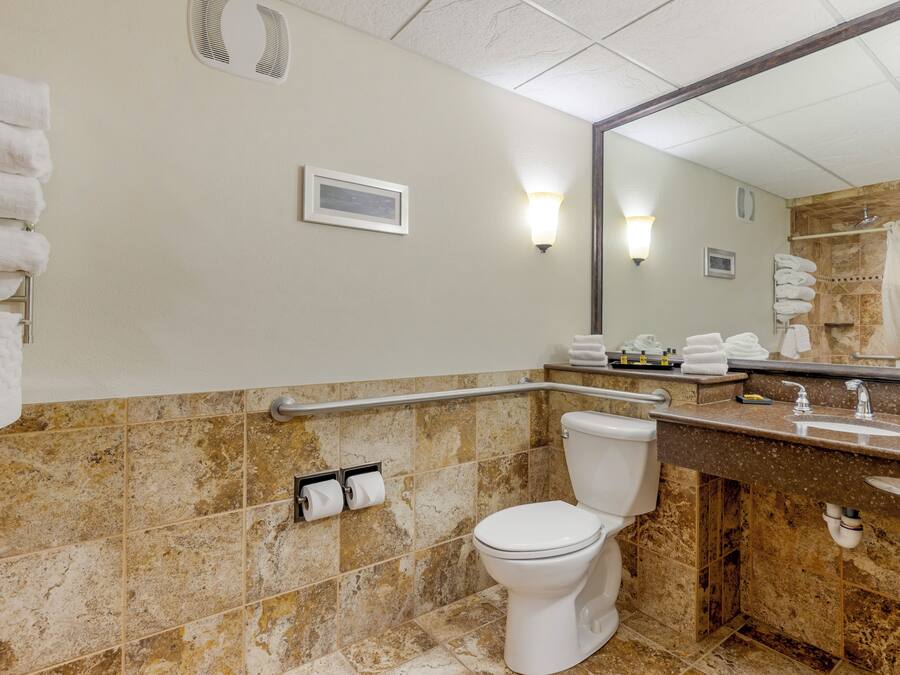 A bathroom with a toilet, sink, and mirror. There are towels stacked on the wall and a shower curtain.