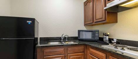 A compact kitchen with a refrigerator, microwave, sink, and stove.