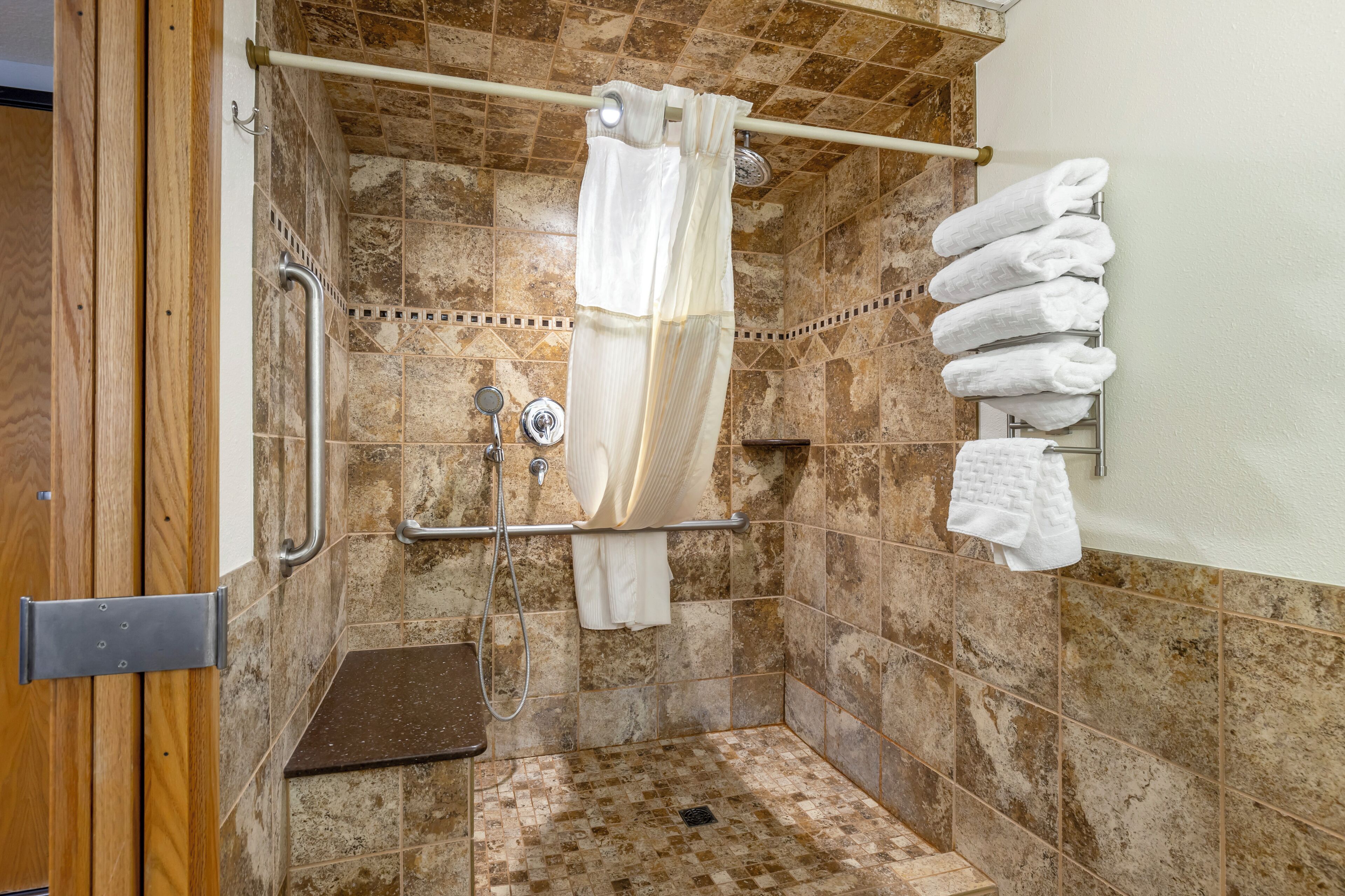 A shower area with a grab bar, a showerhead, and a towel rack with towels.