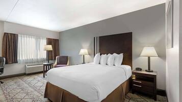 Una habitación de hotel con una cama grande, dos mesitas de noche con lámparas, una silla, un escritorio y una ventana con cortinas.