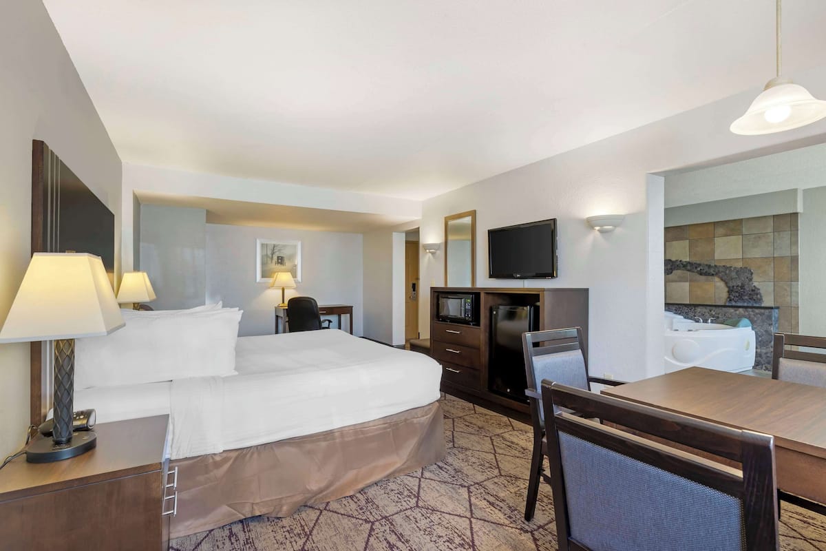 A hotel room with a large bed, a desk with a chair, a television, a microwave, and a small bathroom with a bathtub.