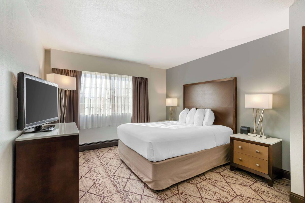 A hotel room with a bed, a TV, a nightstand, and a window with curtains.