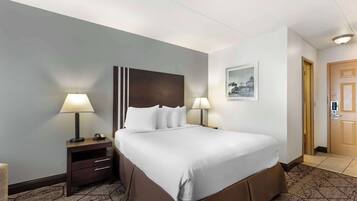 A hotel room with a large bed, two bedside lamps, a nightstand with a lamp, a framed picture on the wall, and a door with a keypad lock.