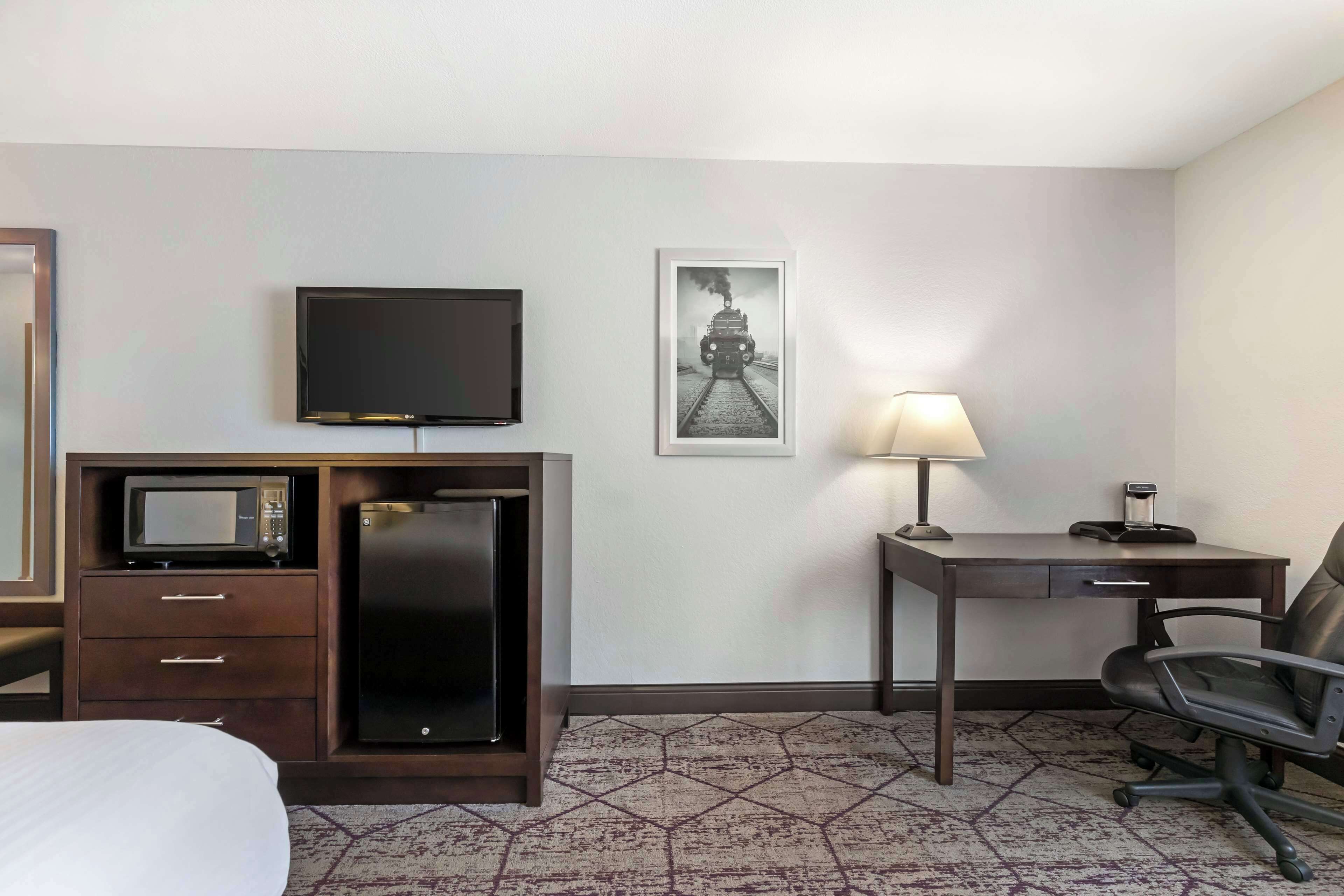 A hotel room with a bed, a desk with a lamp, a television, a microwave, a refrigerator, and a framed picture on the wall.