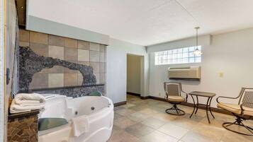 Un baño amplio con una bañera grande, un muro de mosaico de piedra y dos sillas con una mesita.