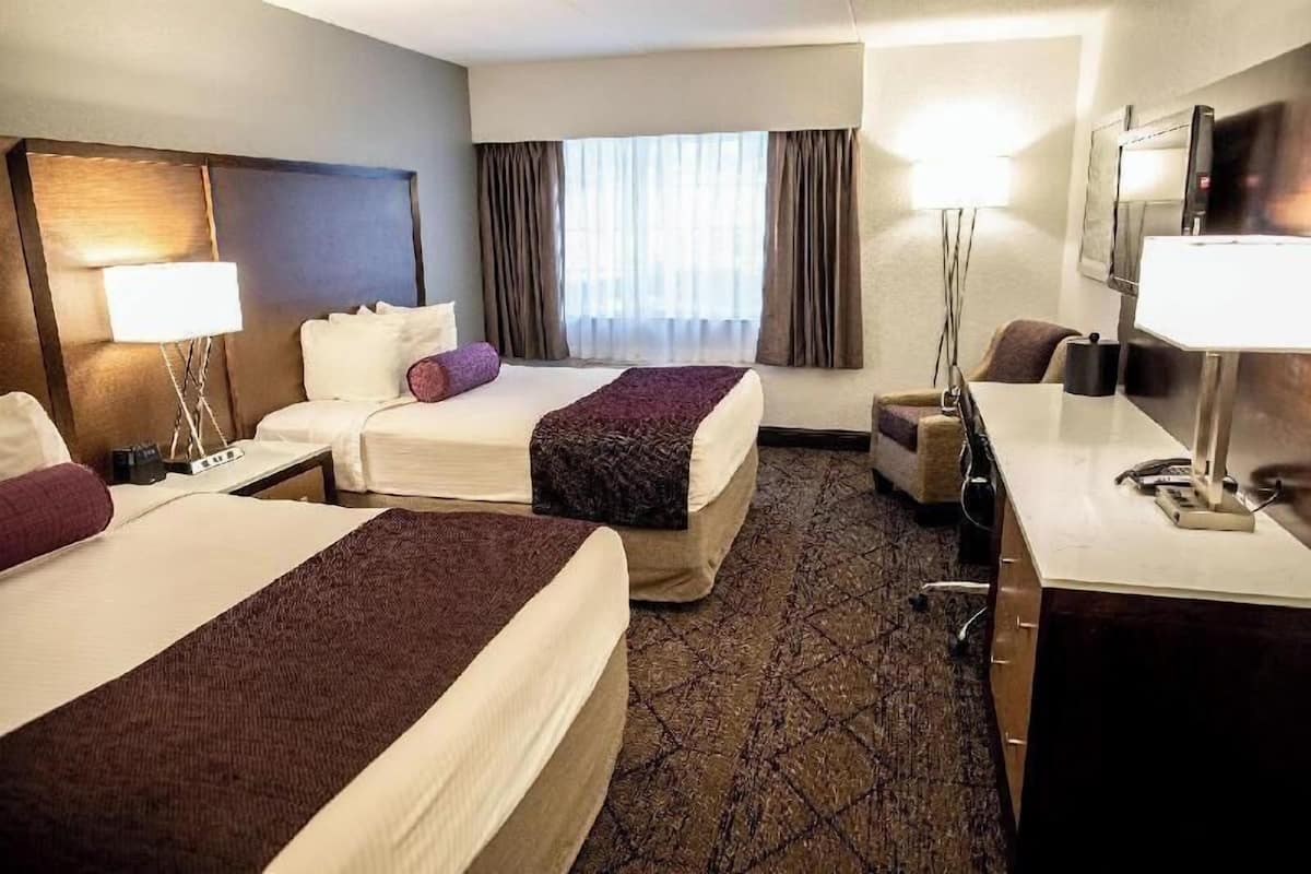 A hotel room with two beds, a desk, a chair, a lamp, a TV, and a window with curtains.