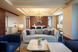 A modern hotel room with a sofa, two armchairs, a coffee table, and a chandelier.