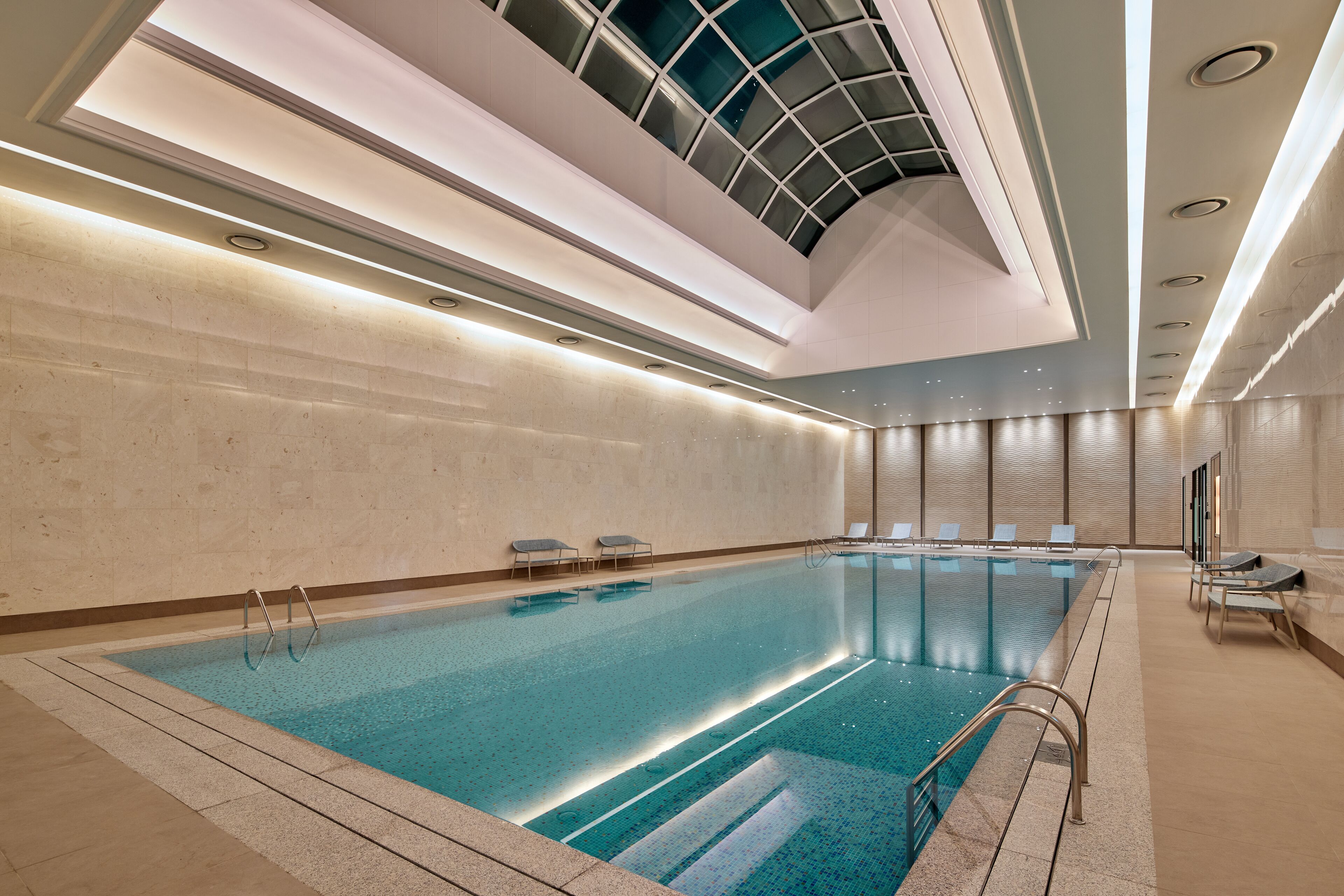 An indoor swimming pool with a glass ceiling, tiled walls, and a modern design.