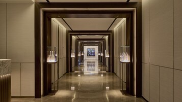 Un largo pasillo bien iluminado con piso pulido, flanqueado por vitrinas de vidrio con jarrones y una obra de arte central.