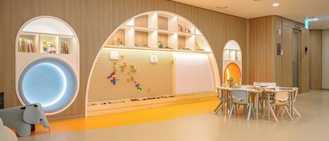A children's play area with a large circular play structure, a pegboard wall with toys, and a seating area with tables and chairs.