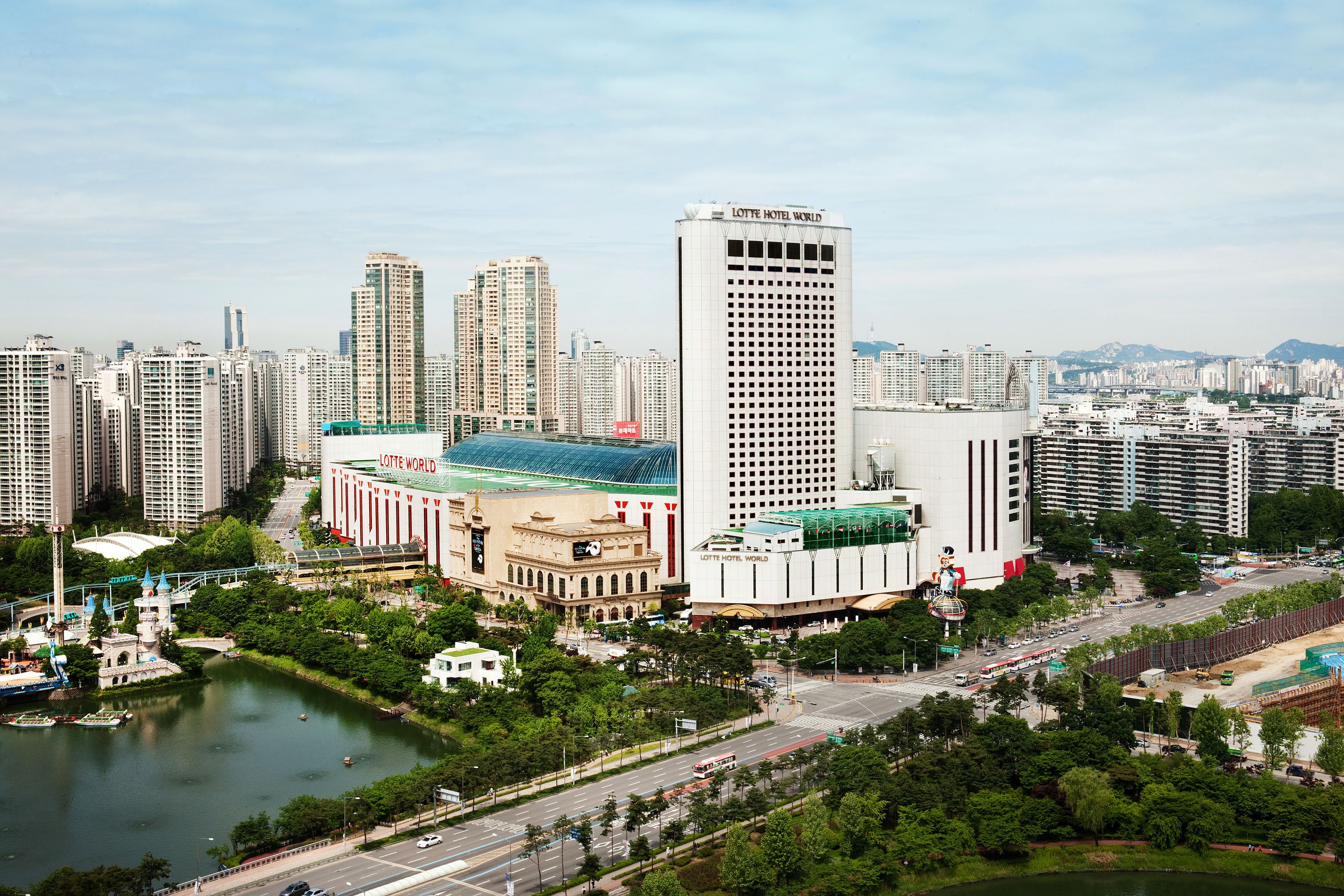 Un paisaje urbano con un destacado edificio Lotte Hotel World, rodeado de rascacielos, un río y un puente.