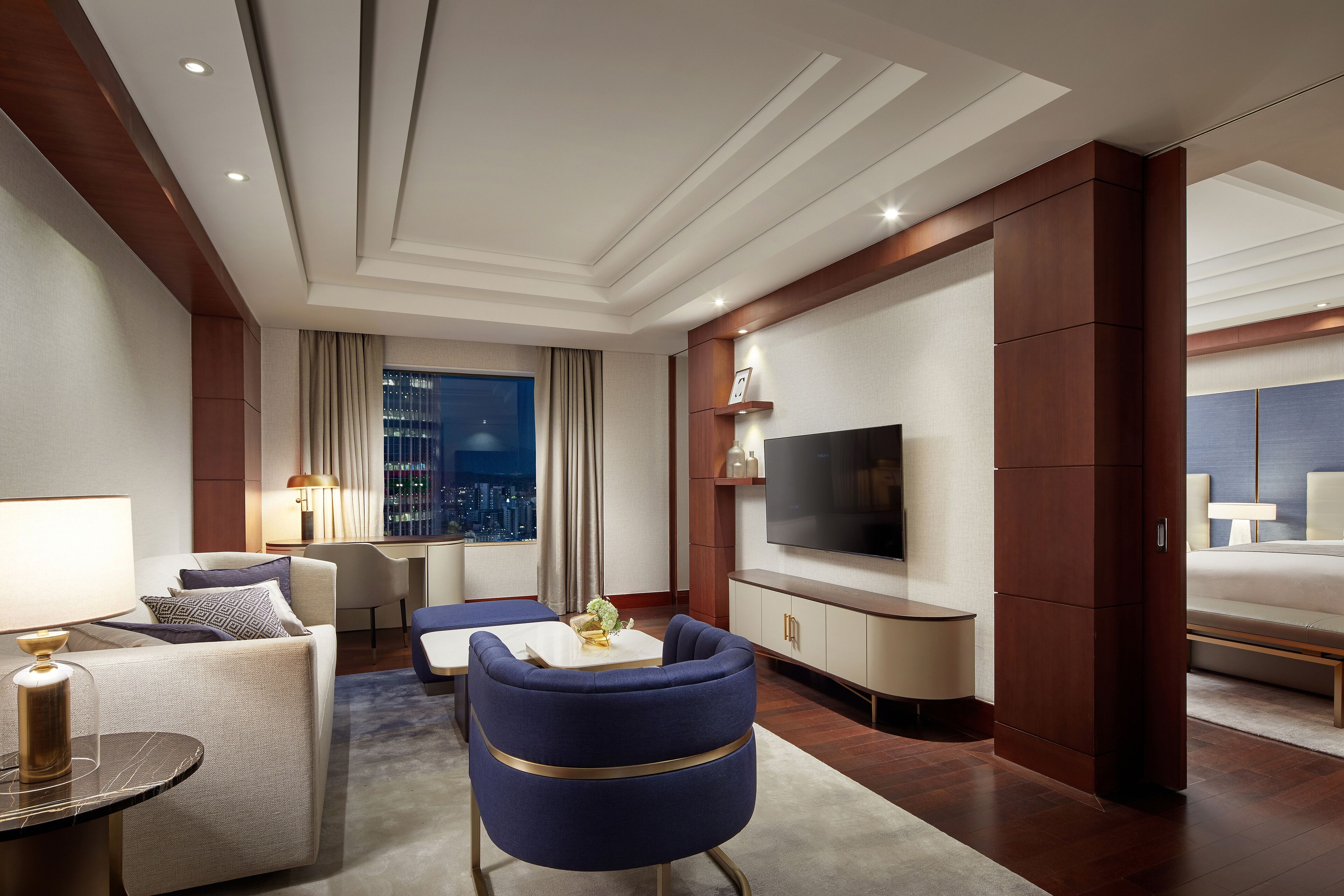Een moderne hotelkamer met een groot bed, een zithoek met een blauwe fauteuil, een televisie en uitzicht over de stad.