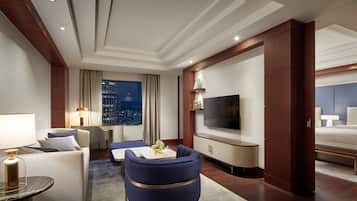 Una habitación de hotel moderna con una cama grande, una zona de estar con un sillón azul, un televisor y vistas a la ciudad.