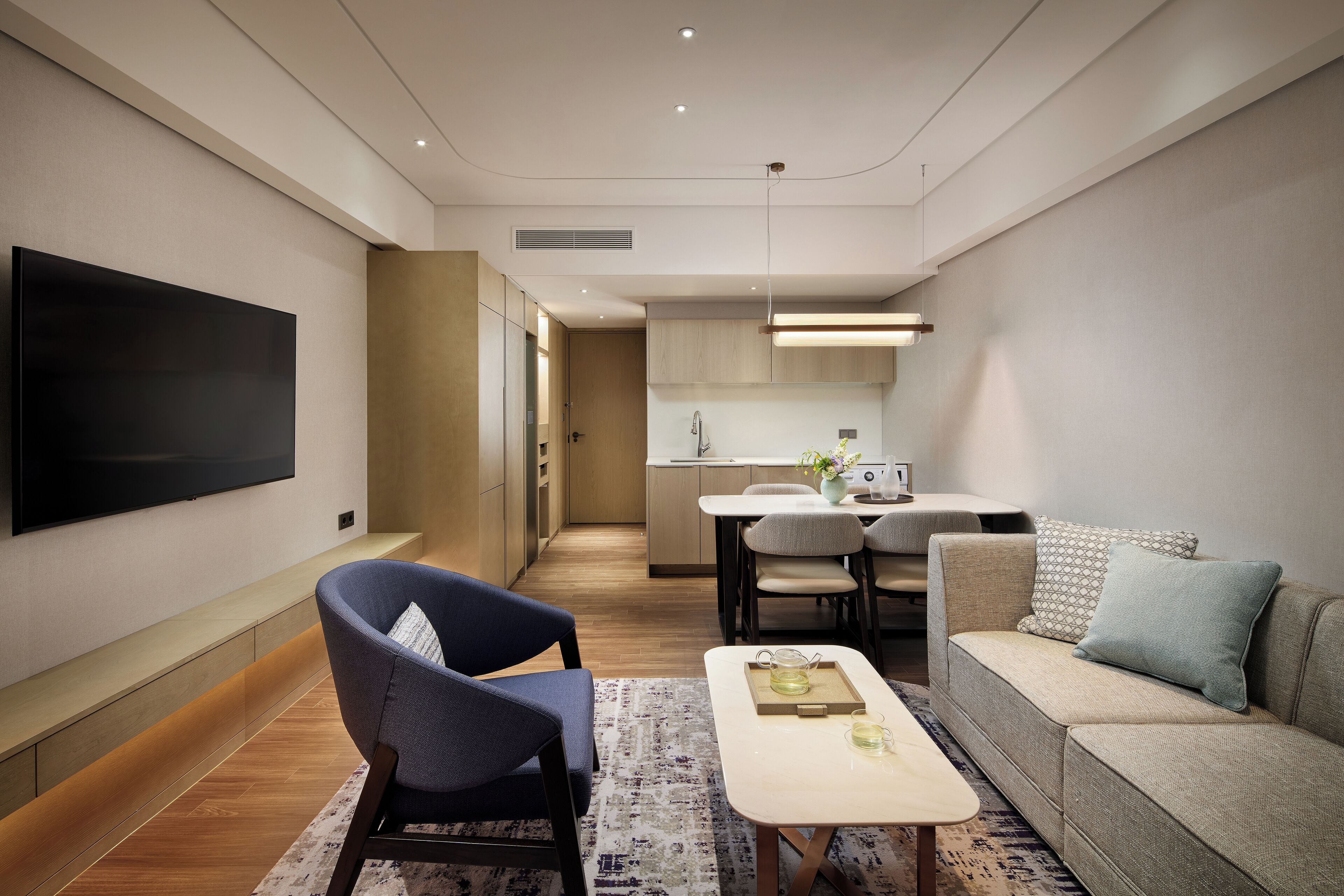 A modern living room with a flat-screen TV, a sofa, a coffee table, and a dining area with a kitchen in the background.