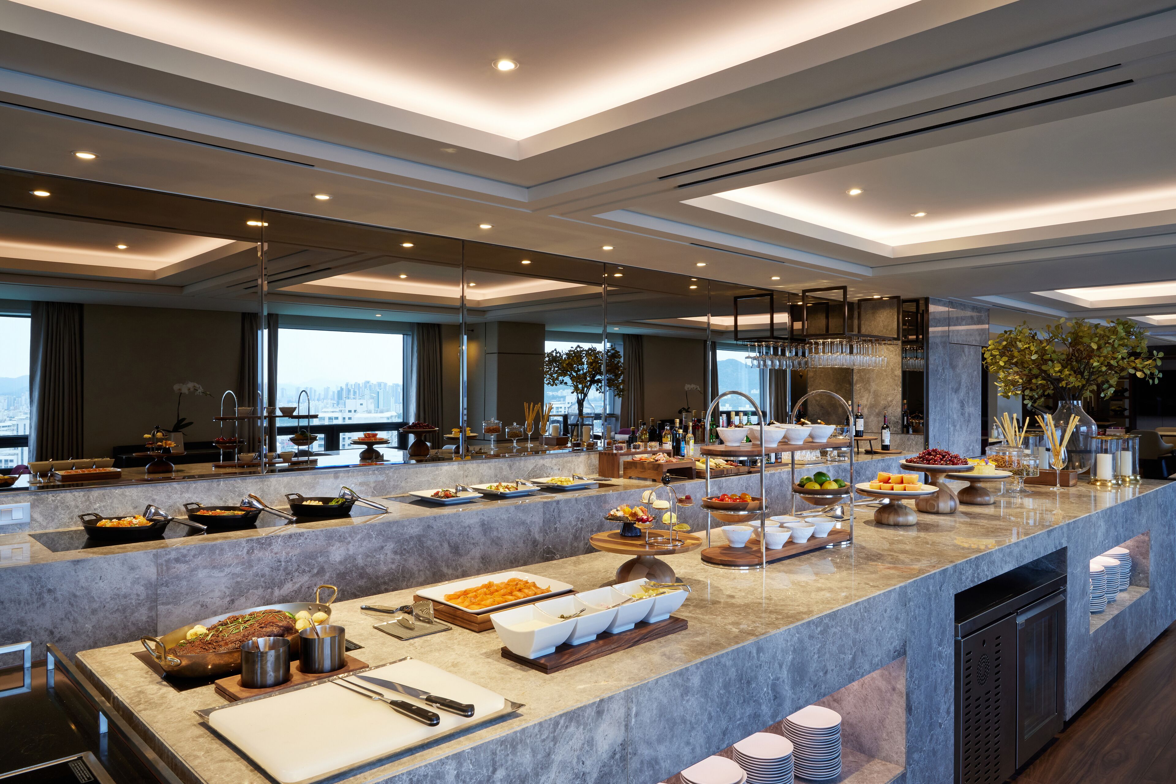 Un buffet de desayuno moderno con diversas opciones de comida, una encimera de mármol y vistas a la ciudad.