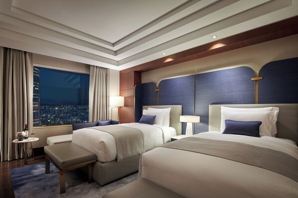 A hotel room with two beds, a city view, a small table with a bottle, and a bench. - Lotte Hotel World (Seoul)