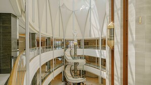 Ein mehrgeschossiges Atrium mit Glasgeländern und einer zentralen Wendeltreppe.