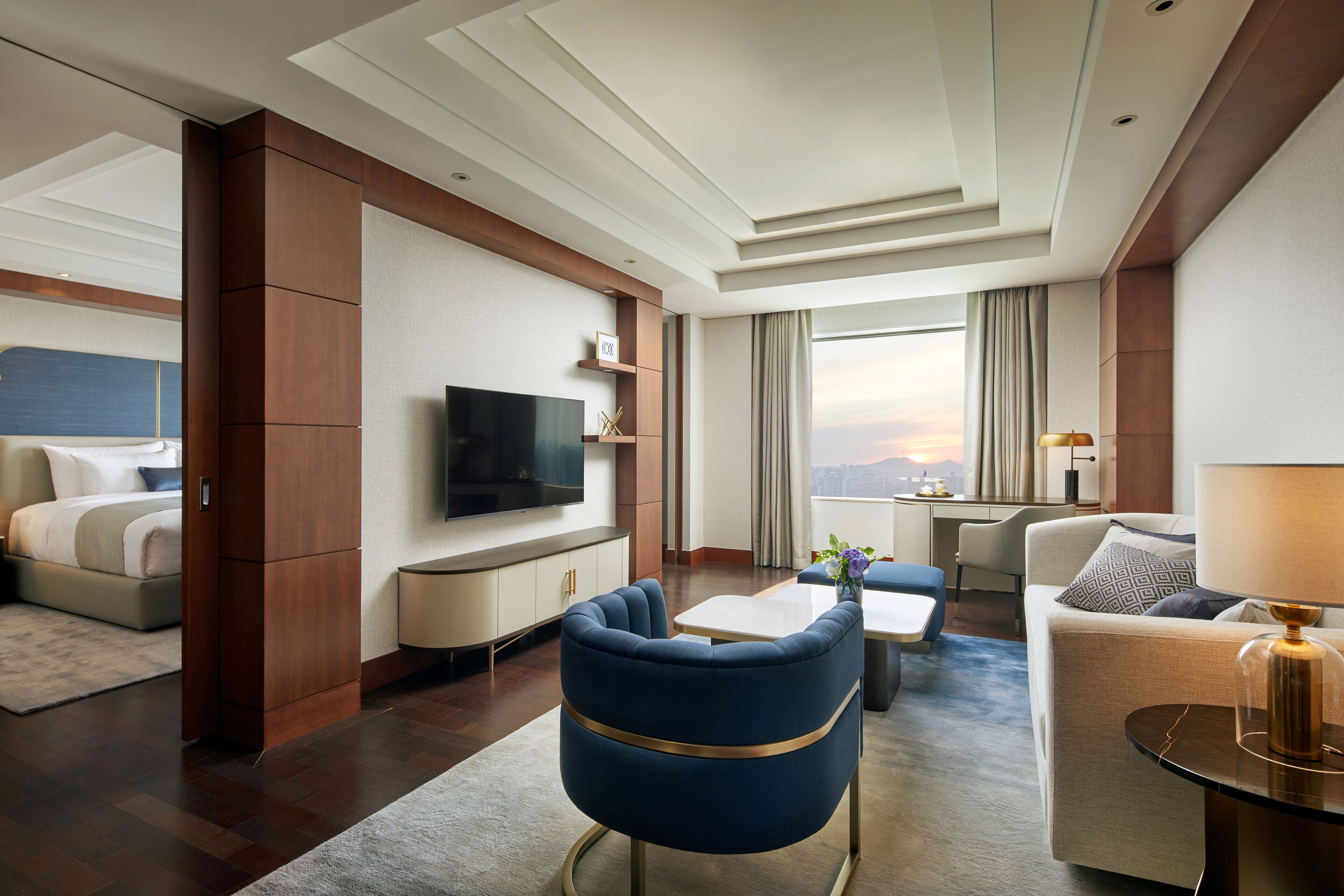 Une chambre d’hôtel moderne dotée d’une télévision à écran plat, d’un canapé, d’une table à manger et offrant une vue sur le paysage urbain.
