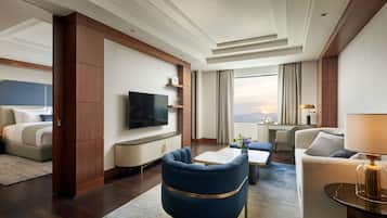 A modern hotel room with a flat-screen TV, a sofa, a dining table, and a view of the cityscape.