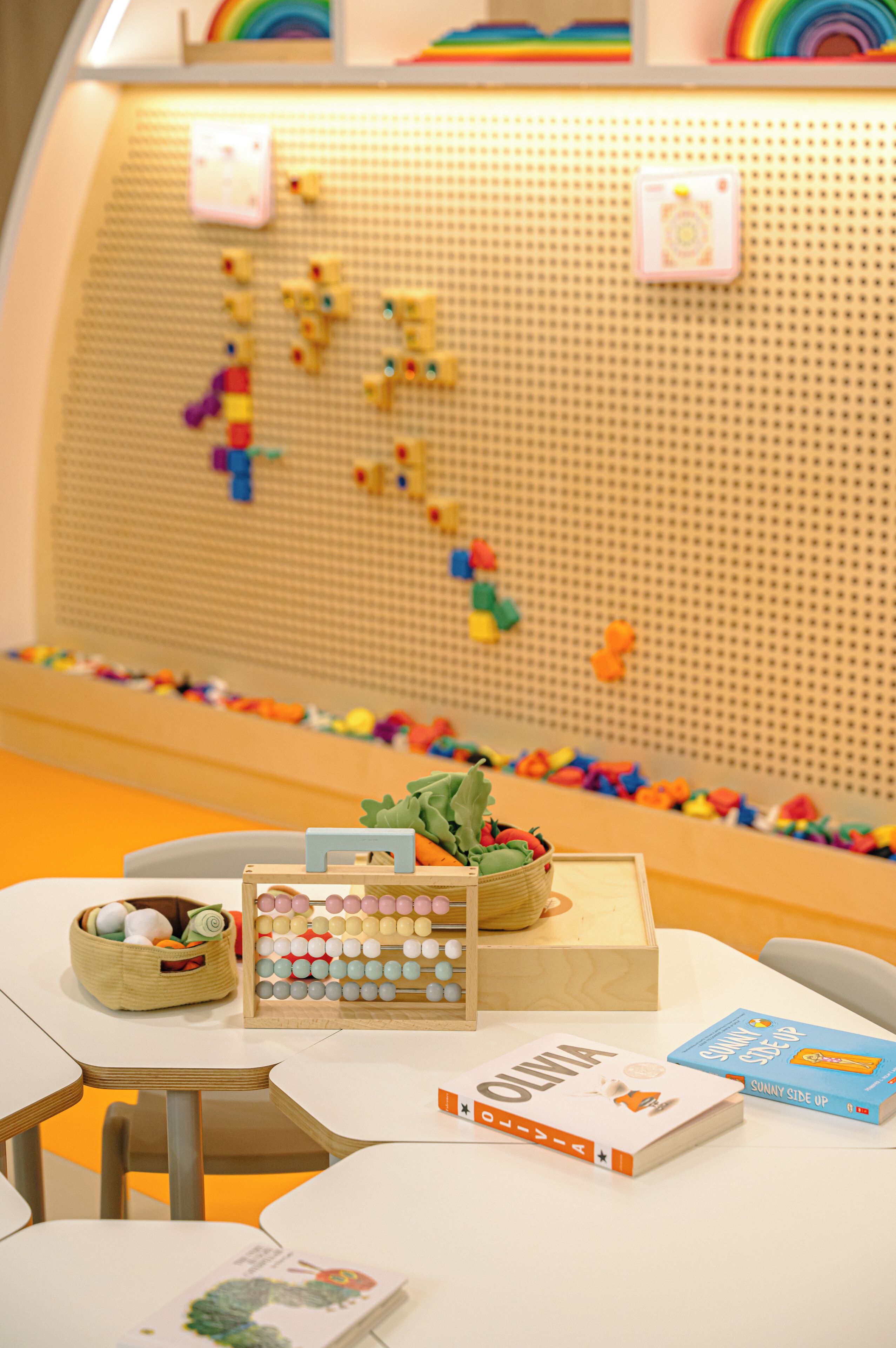 Un área de juegos infantiles con un muro de puzles, un cesto de juguetes y una caja de madera.