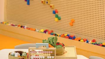 Un área de juegos infantiles con un muro de puzles, un cesto de juguetes y una caja de madera.