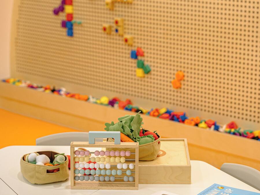 Un área de juegos infantiles con un muro de puzles, un cesto de juguetes y una caja de madera.