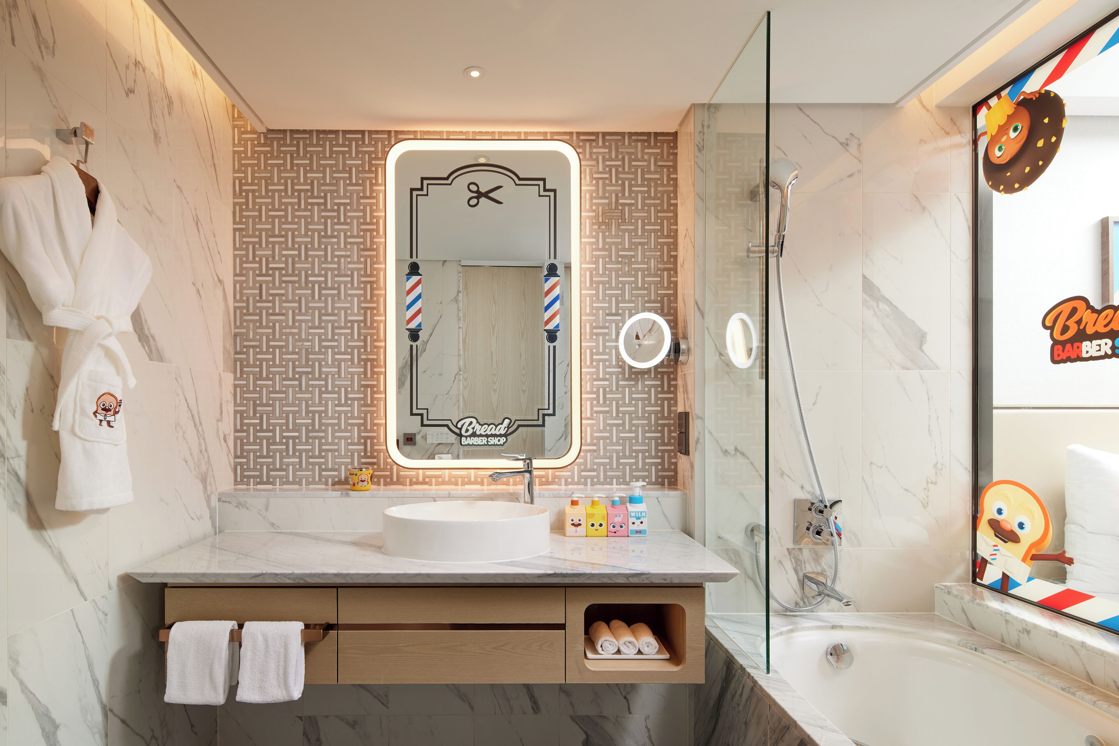 A modern bathroom with a marble sink, a mirror with barber shop branding, and a glass-enclosed shower.