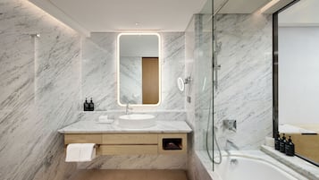 A modern bathroom with a marble wall, a round mirror, a sink, a glass shower enclosure, and a bathtub.