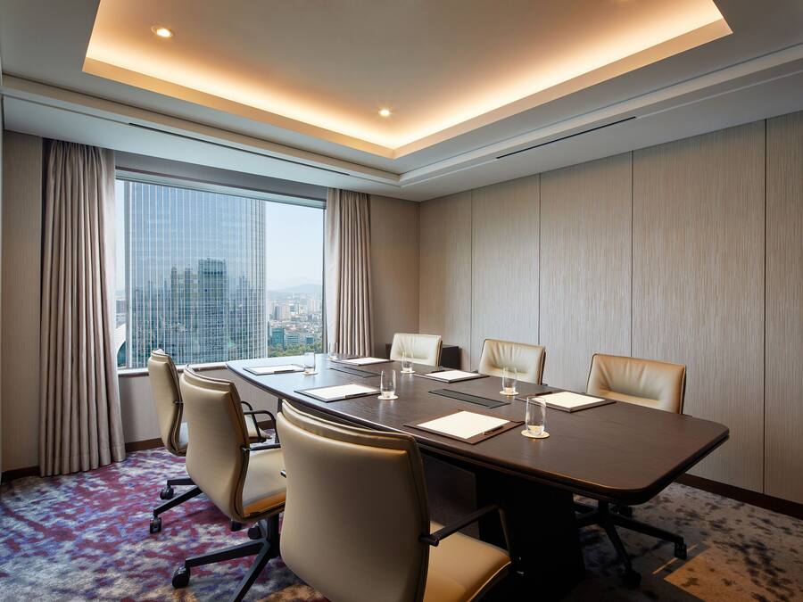 Un salón de conferencias con una gran mesa, seis sillas y vistas a la ciudad a través de amplias ventanas.
