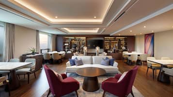 A modern hotel lobby with a central seating area, a dining space, and a kitchen area.