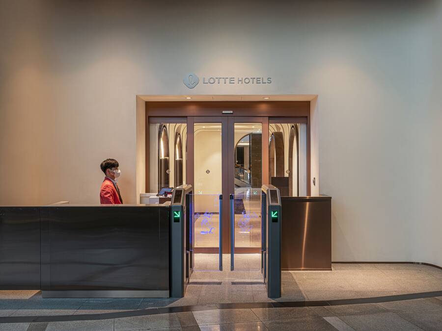 A hotel entrance with a reception desk, a sign reading "LOTTE HOTELS", and a modern interior visible through the glass doors.