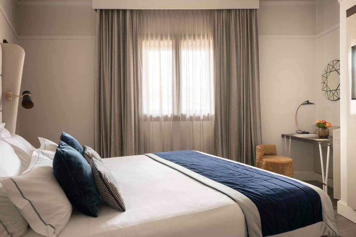 A hotel room with a large bed, a desk, a chair, and a window with curtains.