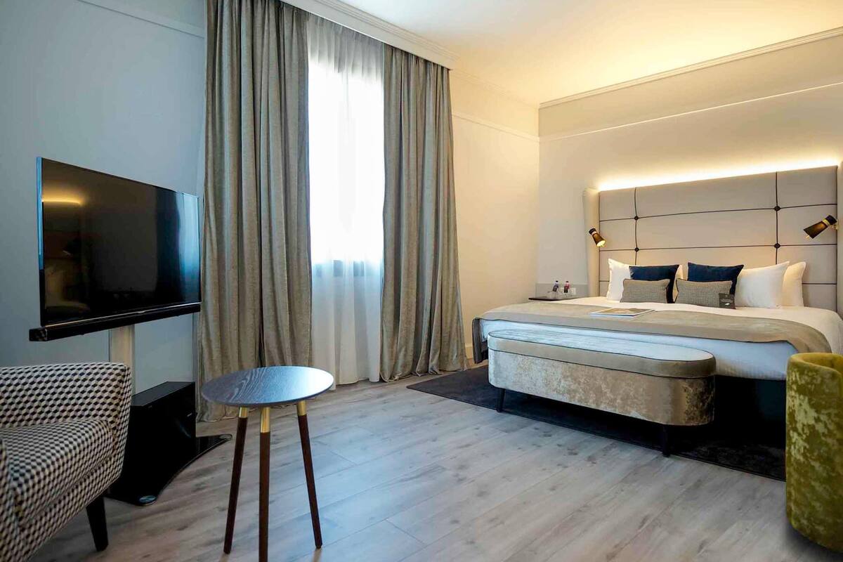 A hotel room with a bed, bedside table, TV, and a small round table.