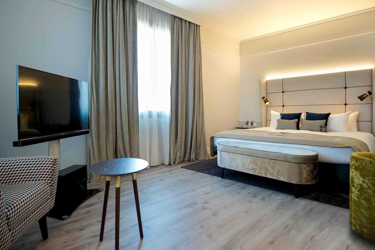 Een hotelkamer met een bed, nachtkastje, televisie en een klein rond tafeltje.