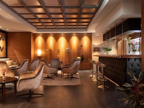 A modern lounge area with a wooden accent wall, a bar with stools, and a seating area with chairs.