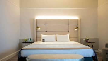 Une chambre d’hôtel moderne avec un grand lit, une table de chevet avec une lampe et une petite table ronde agrémentée d’un vase de fleurs.