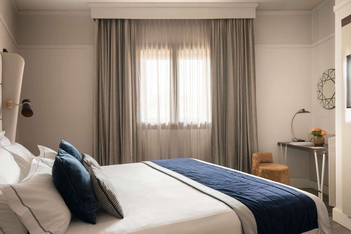 Een hotelkamer met een groot bed, een bureau, een stoel en een raam met gordijnen.