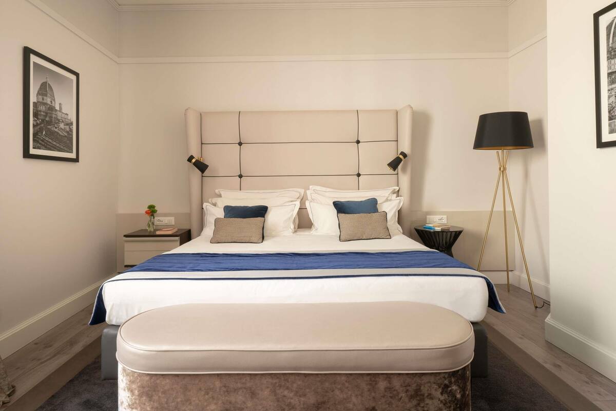 Een keurig opgemaakt slaapkamer met een groot bed, nachtkastjes, een vloerlamp en ingekaderde foto's aan de muur.