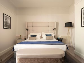 A neatly arranged bedroom with a large bed, bedside tables, a floor lamp, and framed pictures on the walls.