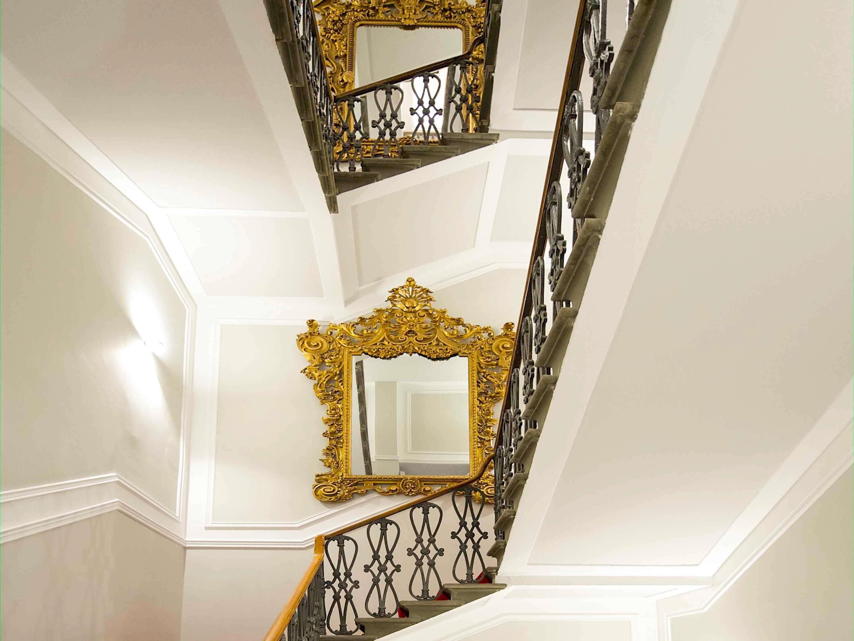 A grand staircase with ornate golden railings and a large mirror with an elaborate frame.
