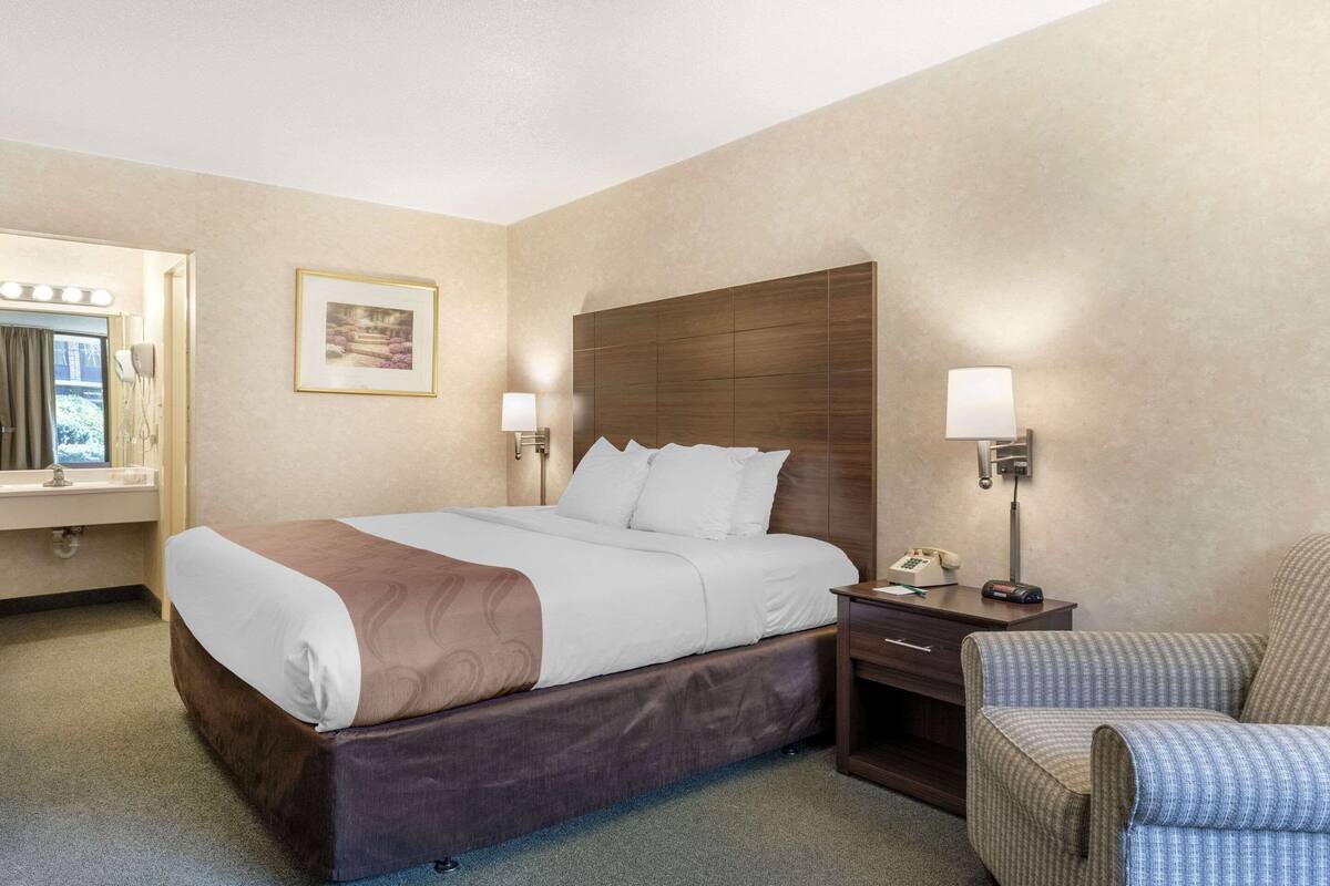 A hotel room with a large bed, bedside lamps, a chair, and a desk with a phone.