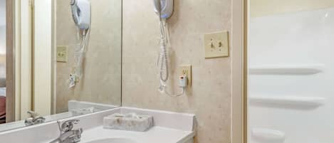A bathroom with a white sink, a mirror, a hairdryer, and a shower.