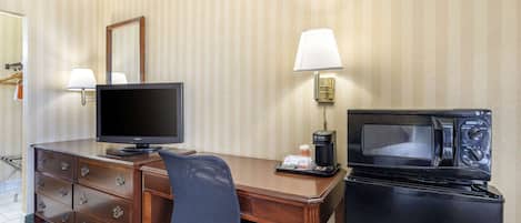 Habitación de hotel con escritorio de madera, televisor, microondas, cafetera y lámpara.