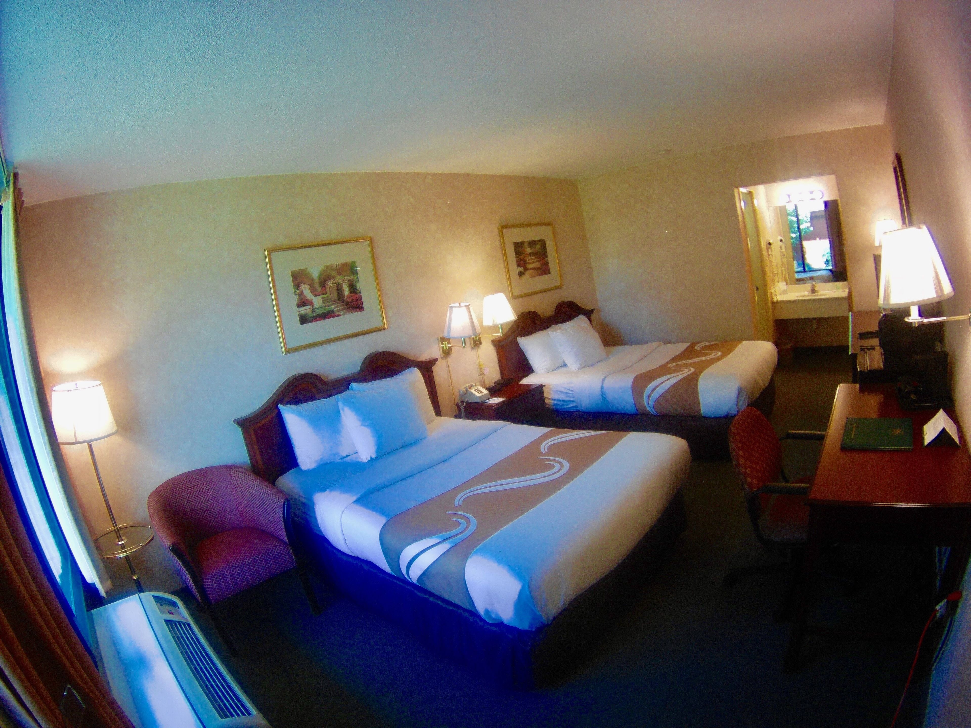 A hotel room with two beds, a desk, a chair, a desk lamp, a telephone, and a television.
