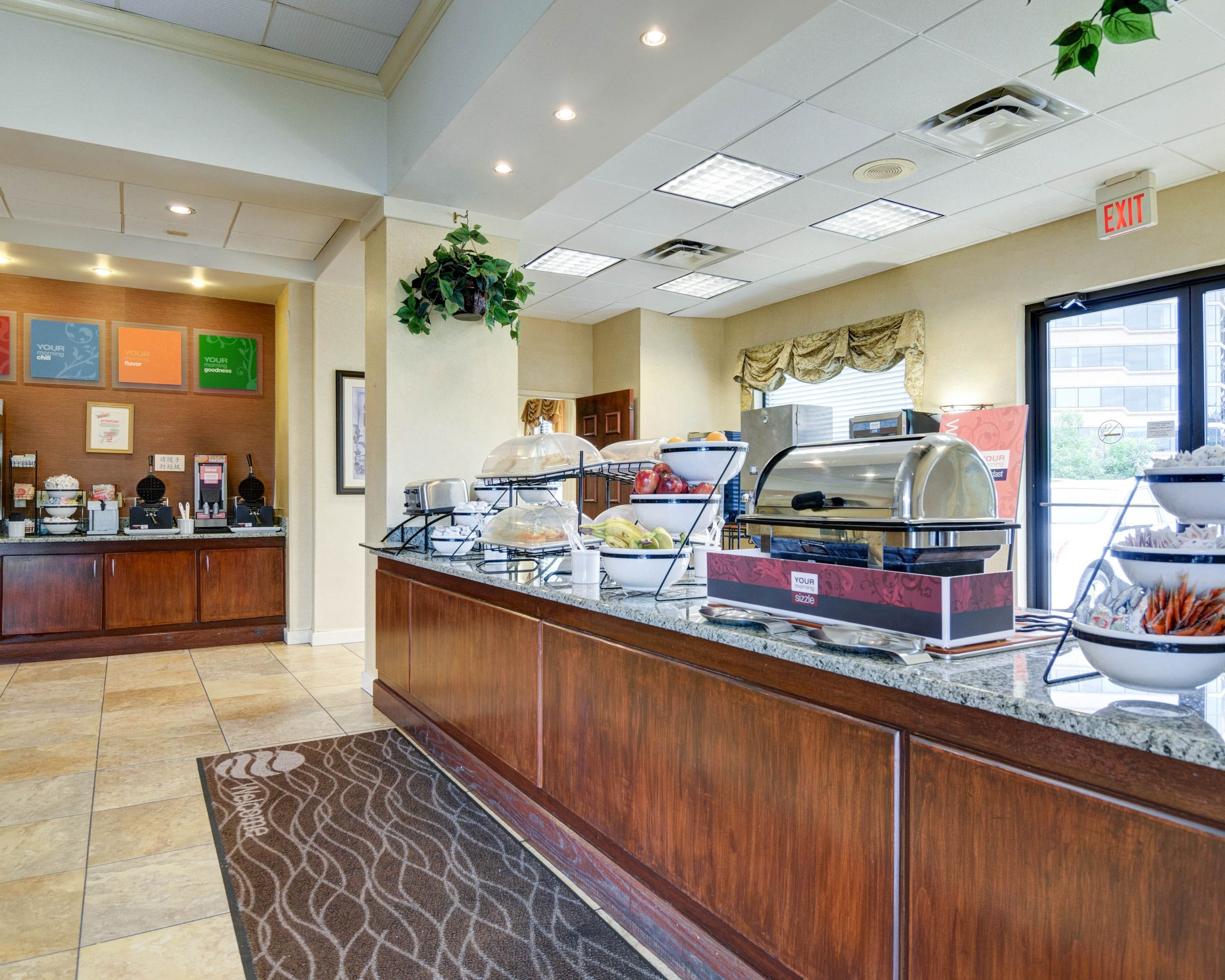 A buffet area with a variety of food stations, including a grill and a salad bar, in a well-lit room with a tiled floor and a welcome mat.
