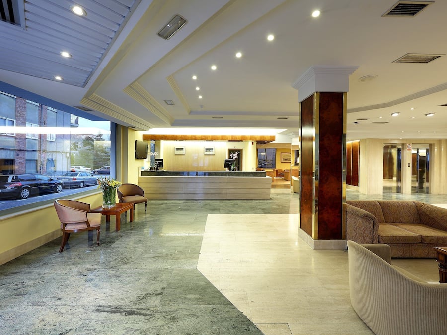 Vestíbulo de hotel con mostrador de recepción, zona de estar y vista a la calle.