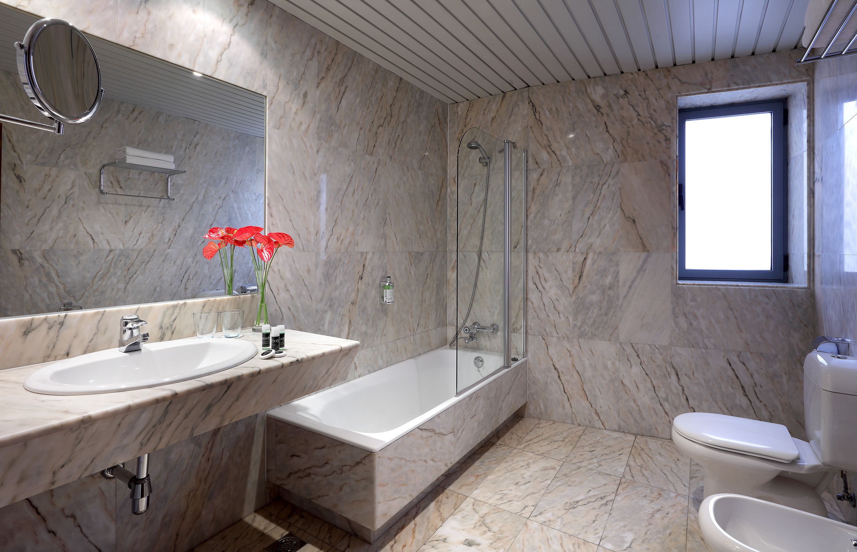 Un baño moderno con paredes de mármol, un espejo grande, dos lavabos, una bañera y un inodoro.