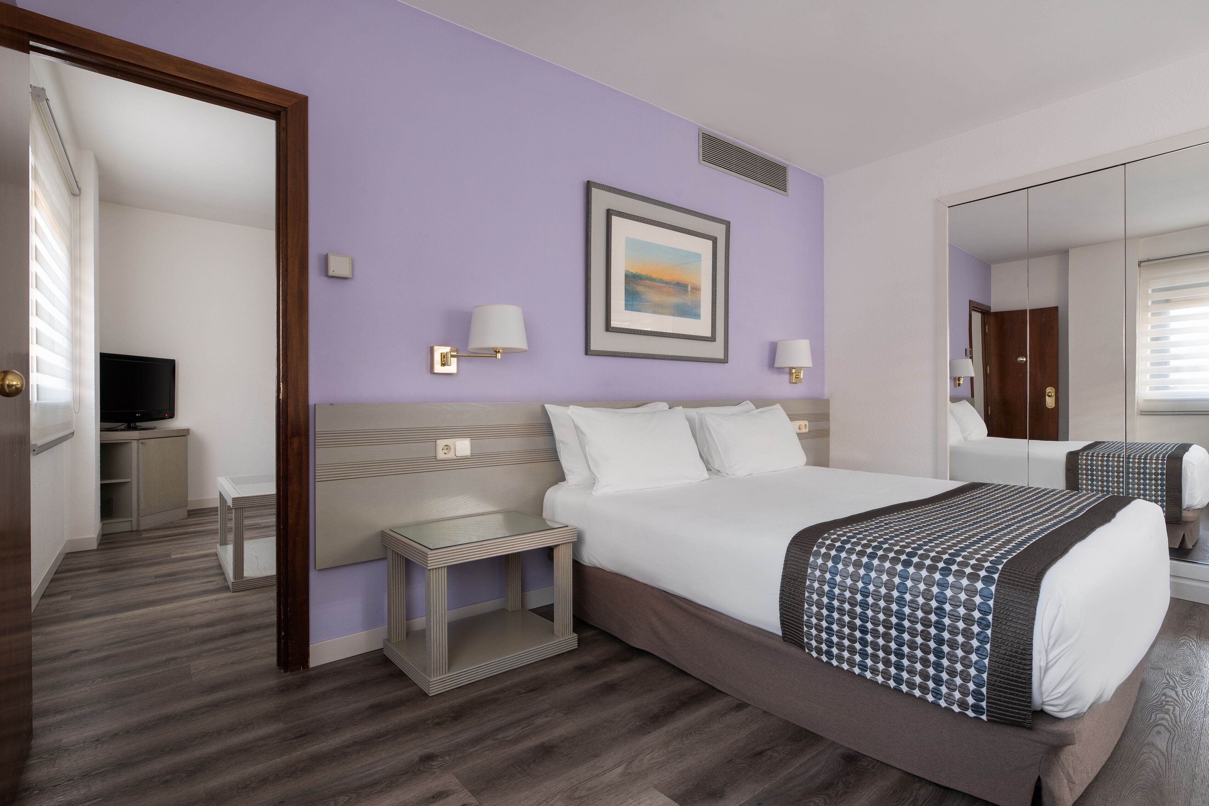 A hotel room with a large bed, a bedside table, a TV, and a mirror.